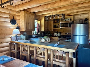 A wooden cabin-style kitchen with a central island, wooden chairs, a stove, and a refrigerator.