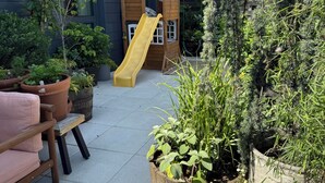A children's play area with a slide, surrounded by potted plants and a wooden bench. - Gorgeous two bedroom with a huge terrace (Brooklyn)