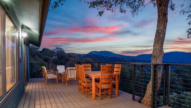 Une terrasse en bois, agréée de mobilier d’extérieur, offrant une vue sur un paysage montagneux au coucher du soleil.