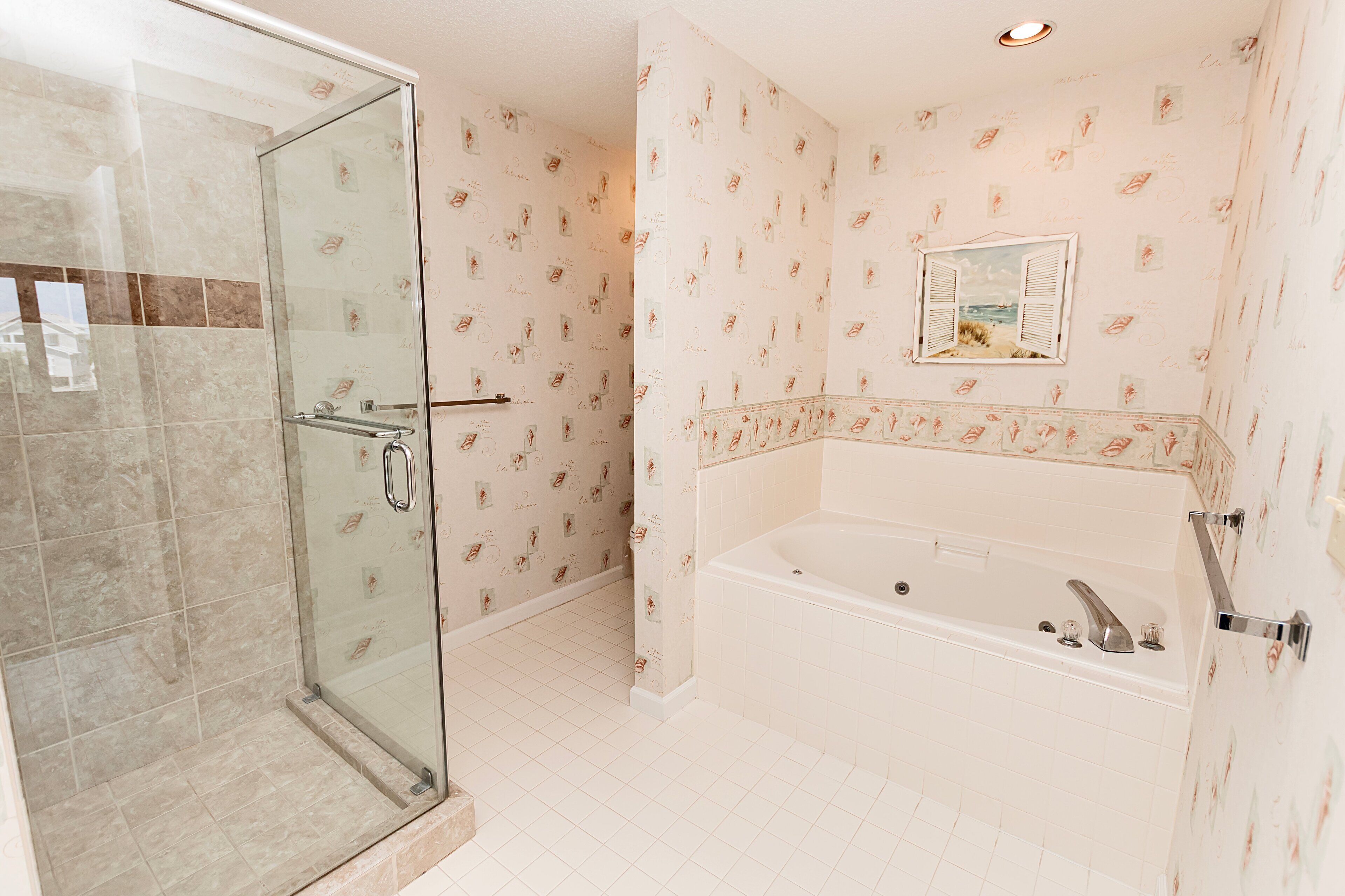 Une salle de bain avec une douche à parois de verre, une baignoire et un papier peint à motifs.