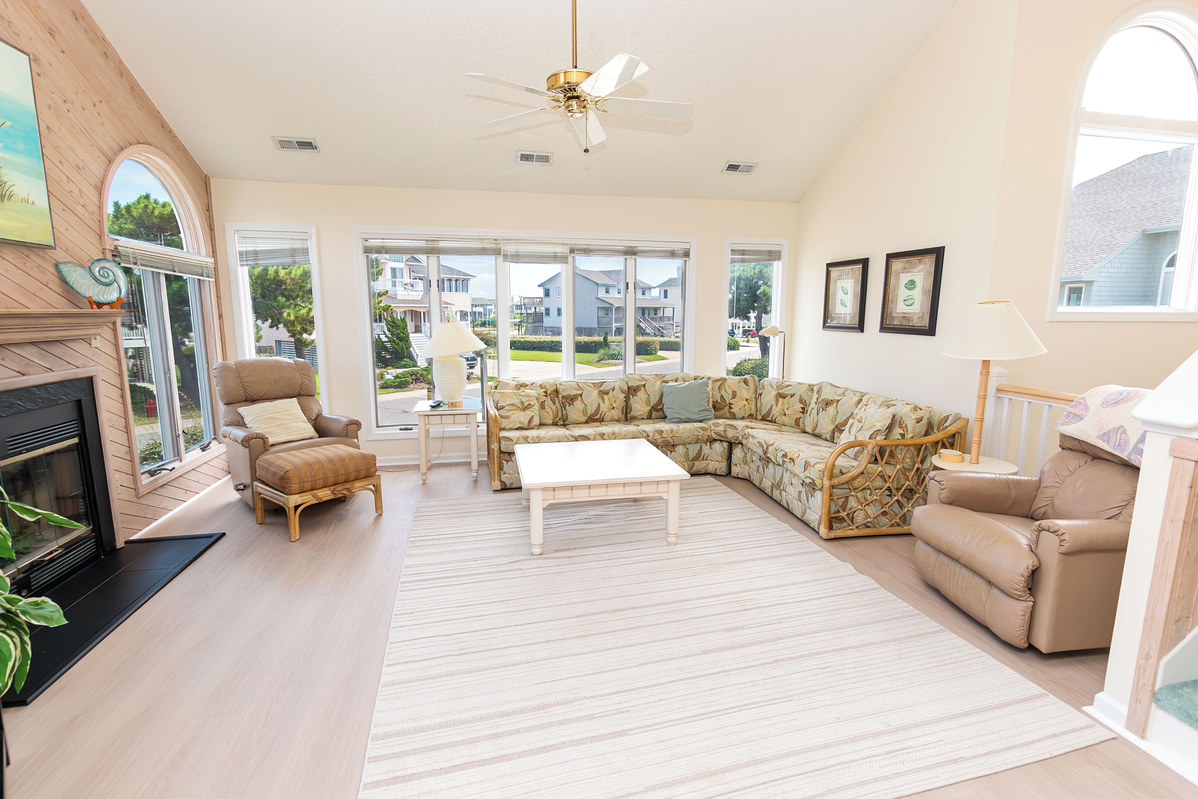 A spacious living room with a fireplace, a sectional sofa, a coffee table, and a ceiling fan.