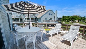 A wooden deck with a round table and chairs, a striped umbrella, and a view of residential buildings in the background. - Oceanside, Community Pools, Community Tennis, 628,  Corolla Time (Corolla)
