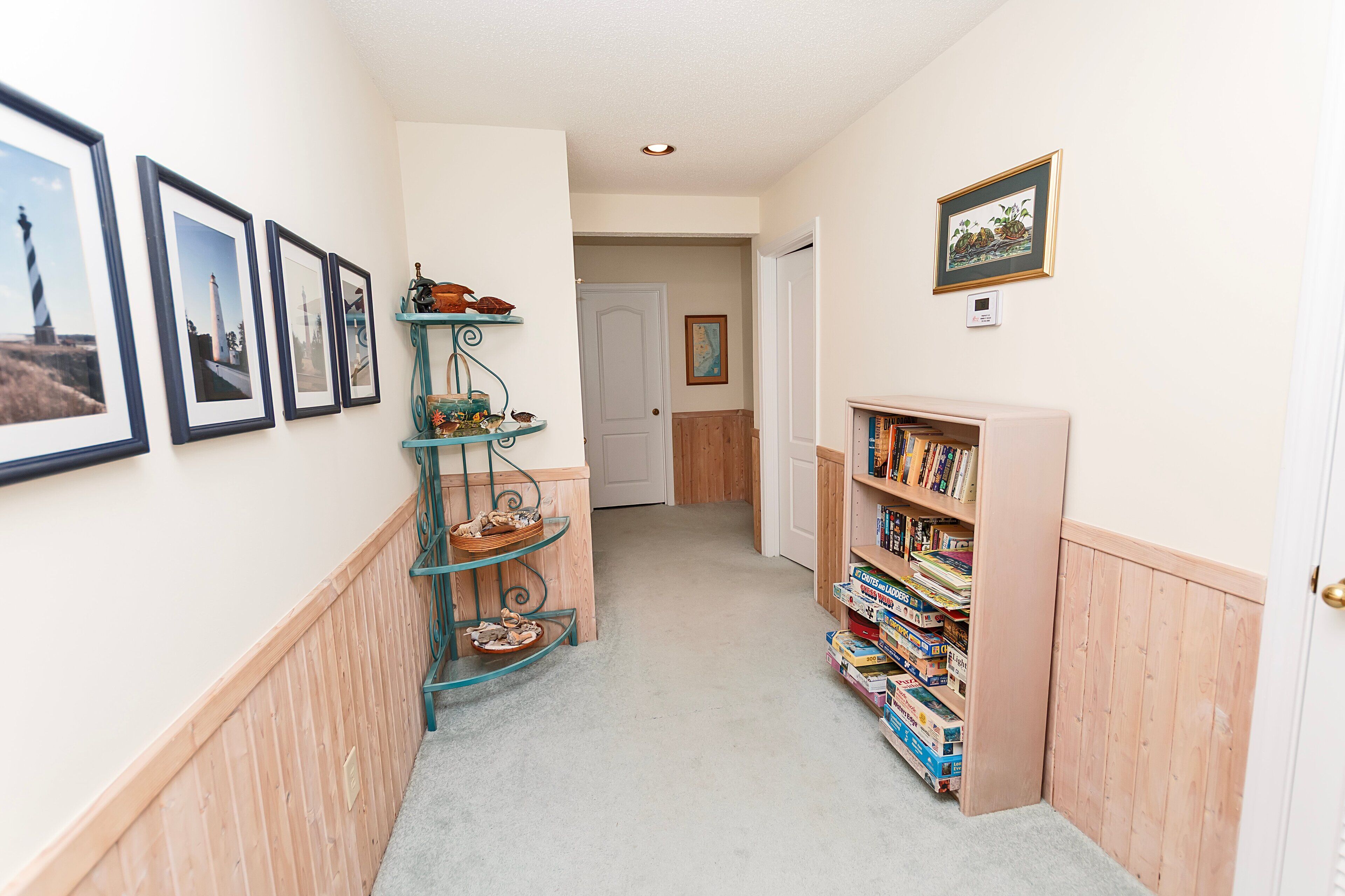 A hallway with framed pictures, a wooden shelf with decorative items, and a bookshelf filled with books.