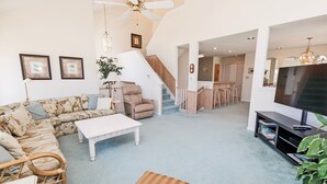 A spacious living room with a sectional sofa, a coffee table, and a TV stand with a flat-screen TV. There is a staircase leading to an upper level. - Oceanside, Community Pools, Community Tennis, 628,  Corolla Time (Corolla)