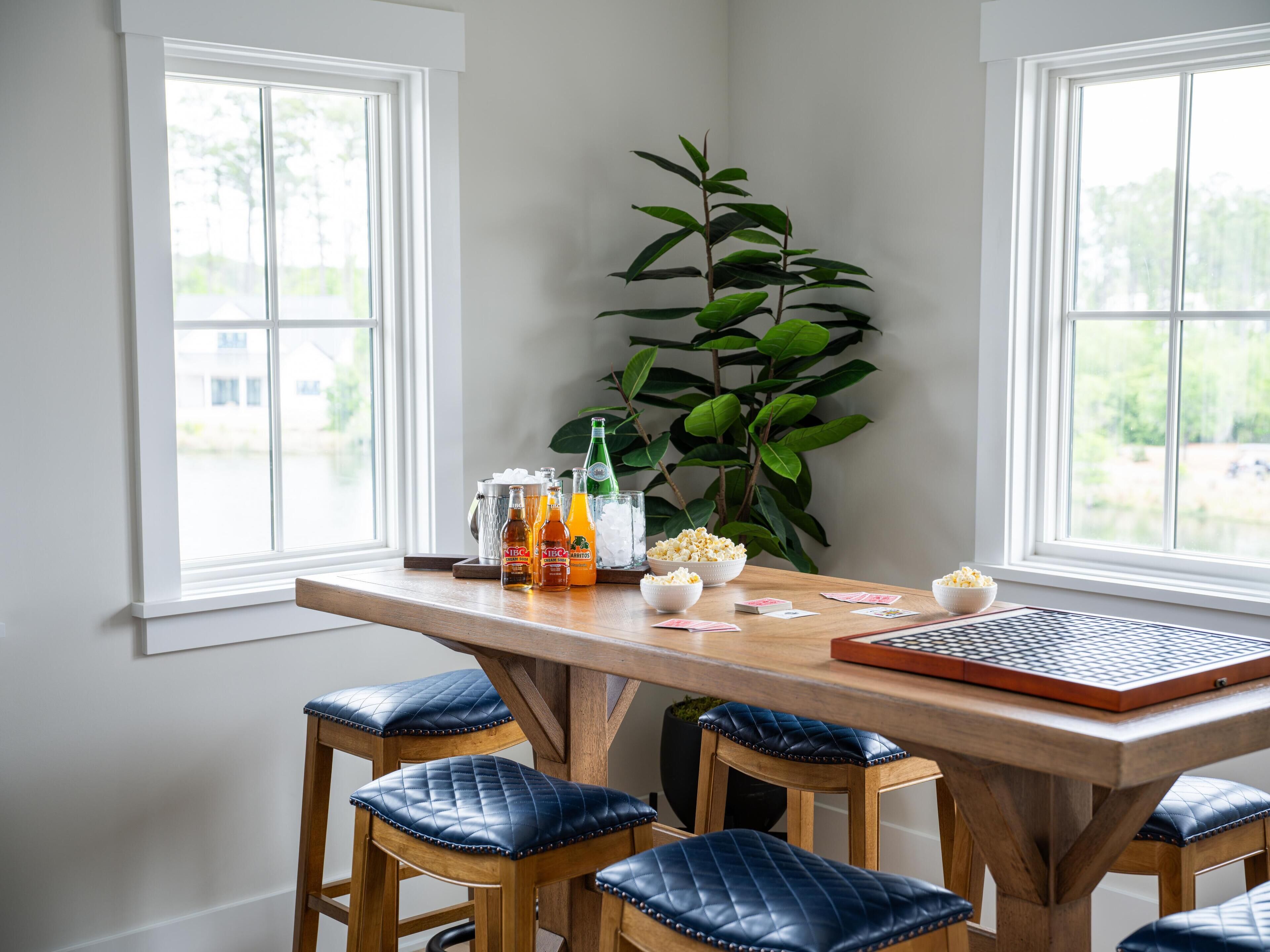 Un comedor con una mesa de madera, cuatro sillas azules acolchadas, una planta y un tablero de ajedrez.