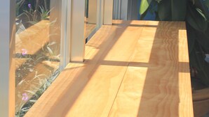 Une table en bois avec un panneau de verre, une plante en pot et une vue sur un jardin à travers le verre.