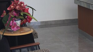Un espace d’accueil comprenant une horloge, un miroir, un vase à fleurs et un coin salon avec une table et des chaises.