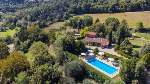 Eine Villa mit Swimmingpool, umgeben von üppiger Vegetation und einer hügeligen Landschaft.