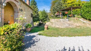A stone building with an arched entrance, a gravel path, and a garden area with potted plants and a pergola. - Focolare by Interhome (Trequanda)