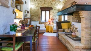 A rustic interior with a stone wall, wooden beams, a dining table with chairs, a sofa, and a fireplace. - Focolare by Interhome (Trequanda)