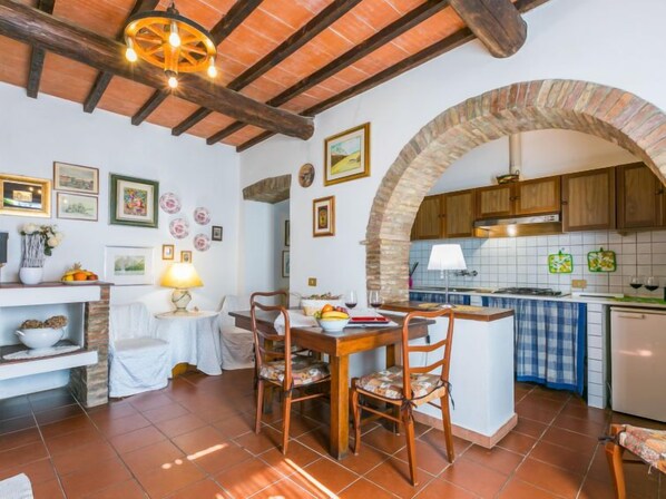 A cozy kitchen with a rustic wooden ceiling, a stone archway, and a tiled backsplash.