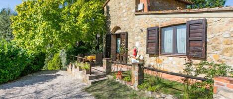 A stone house with a gravel driveway, wooden shutters, and a small outdoor seating area.