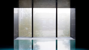 Ein modernes Interieur mit spiegelndem Boden, einem großen Fenster mit vertikalen Jalousien und einer Betonwand.