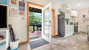 Une cuisine moderne avec des meubles blancs, un réfrigérateur noir et une terrasse en bois visible à travers la porte ouverte.