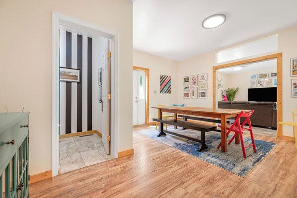 A spacious living room with a wooden floor, a dining table with chairs, a sofa, and a TV.