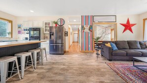 Une cuisine moderne avec un coin bar, un espace repas doté d’un canapé et un couloir menant à une chambre.