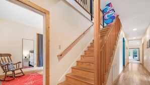 Un escalier en bois avec une rampe, un tapis rouge à motifs et un fauteuil à bascule dans un couloir au plancher en bois.