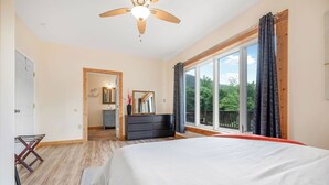 Une chambre avec un grand lit, un ventilateur de plafond, une commode et une vue sur l’extérieur grâce à une grande fenêtre.