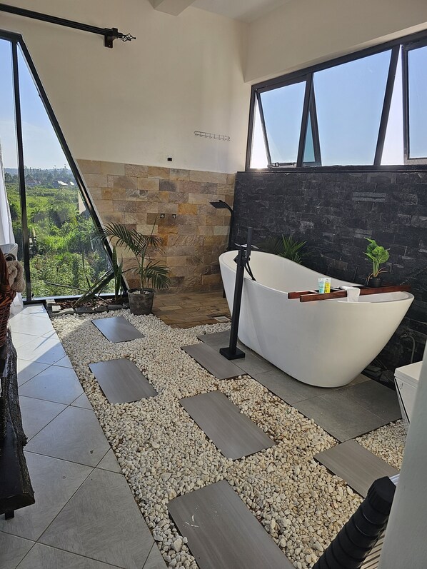 Un baño moderno con una bañera independiente, paredes de piedra y vista a zonas verdes.