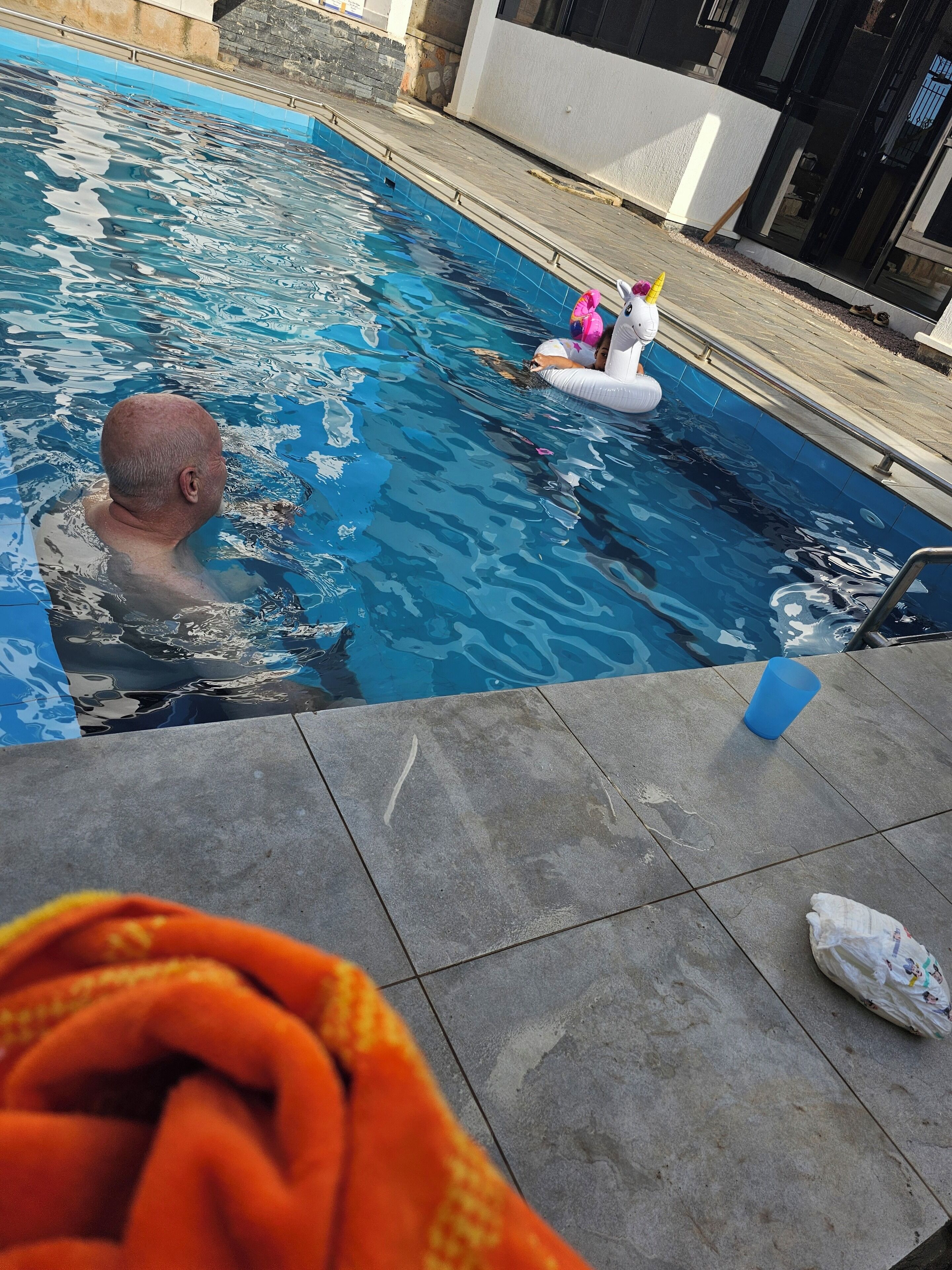Une piscine avec une terrasse carrelée, une personne dans l’eau et un jouet flottant.
