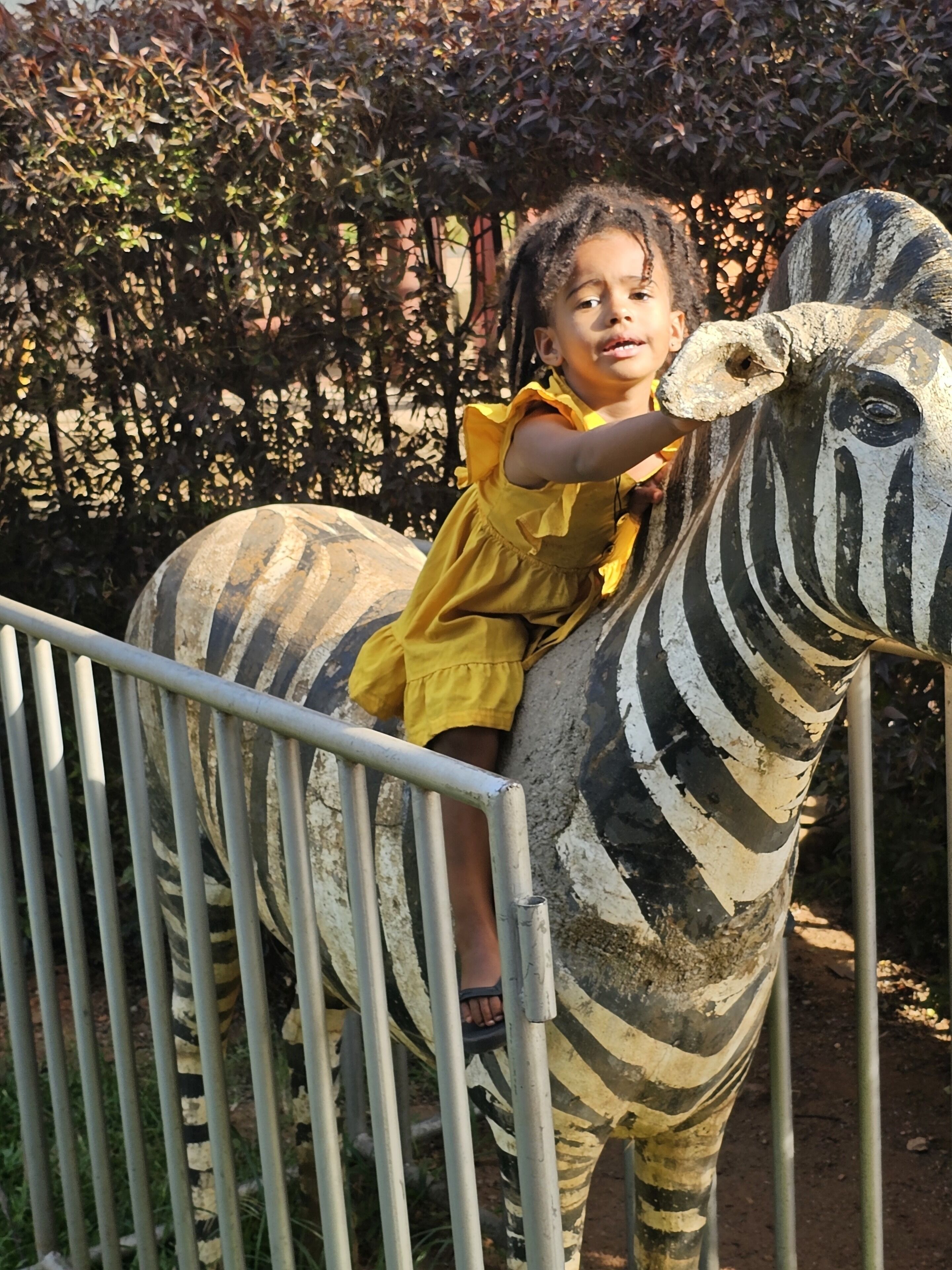 Een kind in een gele jurk zit op een zebrabeeld.