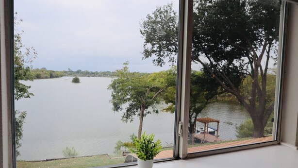 A view through a window with a potted plant on a white surface. - 5BR Near AT&T Stadium Lakefront Sleeps 10 Best Lake Views at Irving Lake (Irving)