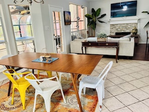 Un área de comedor con una mesa y sillas de madera, un televisor montado en la pared y una planta grande.