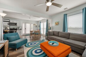 A modern living room with a grey sofa, teal armchair, and orange ottoman.