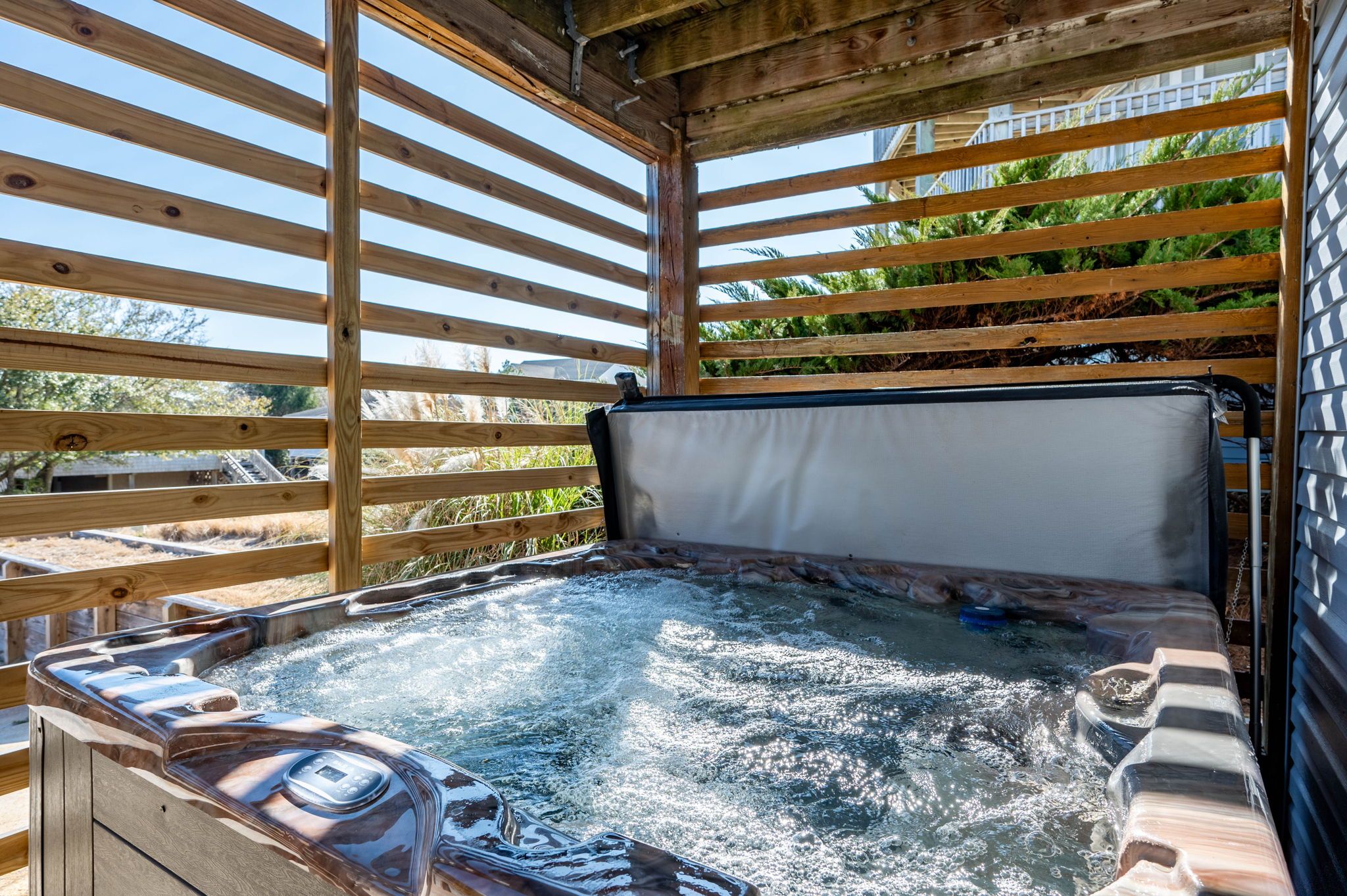 A hot tub with a wooden frame and a digital control panel, surrounded by a wooden deck and a view of greenery.