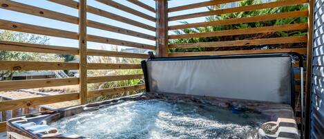A hot tub with a wooden frame and a digital control panel, surrounded by a wooden deck and a view of greenery.