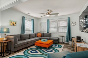 A modern living room with a sectional sofa, a coffee table, a lamp, a ceiling fan, and a rug. - Good Vibes Soundside: Cute, Soundside Home, Short Stays anytime with Hot Tub! (Kill Devil Hills)