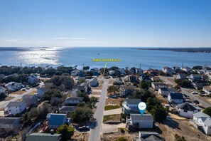 Vue aérienne d’un quartier résidentiel situé sur la côte, avec des maisons, un ciel bleu dégagé et une étendue d’eau en arrière-plan.