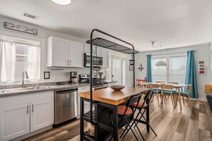 Cocina moderna con gabinetes blancos, lavavajillas, microondas y cafetera. Cuenta con un comedor con mesa y sillas.