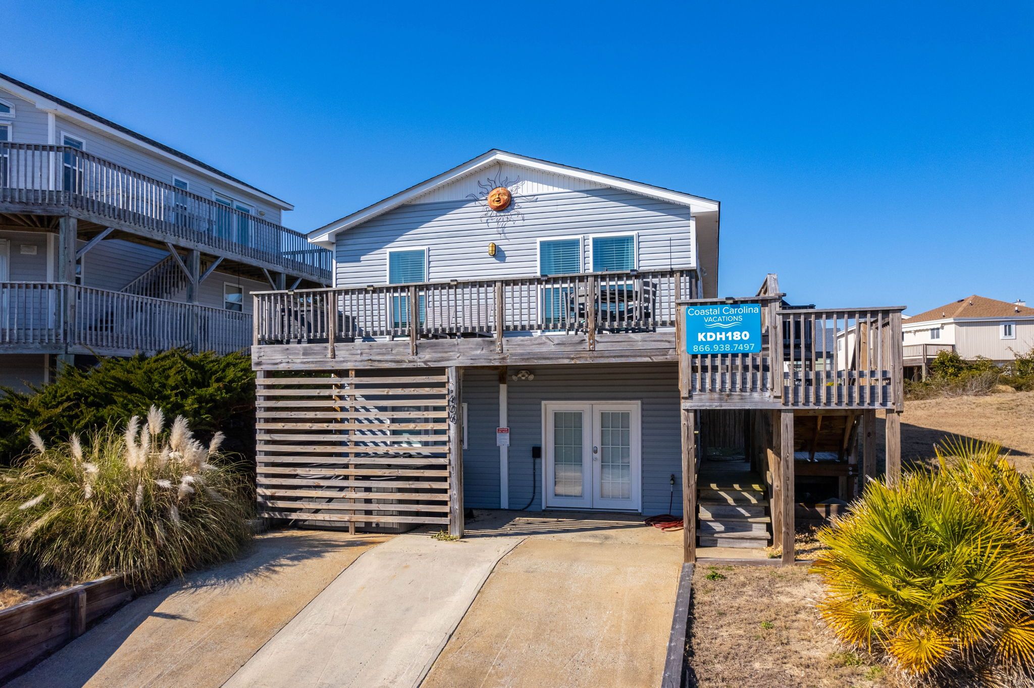 Un bâtiment à deux étages situé sur la côte, doté d’un balcon, d’un garage et d’une enseigne publicitaire pour l’entreprise Coastal Carolina Vacations.