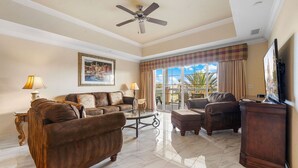 A spacious living room with a ceiling fan, a large window with curtains, and a television on the right.