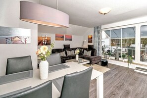 Een moderne woonkamer met een bank, salontafel en een eethoek. Grote ramen bieden uitzicht op het omliggende landschap.