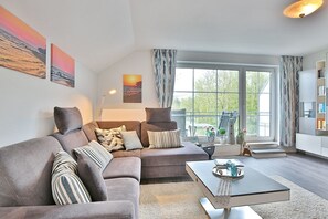 Un salon moderne avec un canapé d’angle gris, une table basse et une grande fenêtre agrémentée de rideaux.