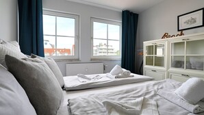 A hotel room with a bed, a chest of drawers, a radiator, and a window with curtains. - Seesternresidenz Appartement 21 - Seesternresidenz (Scharbeutz)