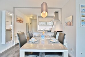 Un comedor moderno con una mesa grande dispuesta para seis personas, una lámpara colgante y una cocina al fondo.