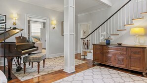Um piano de cauda em uma sala de estar ampla, com piso de madeira e escada branca.