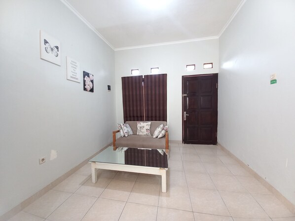 A room with a glass-top table, a sofa with floral cushions, a dark door, and a wall with framed pictures.