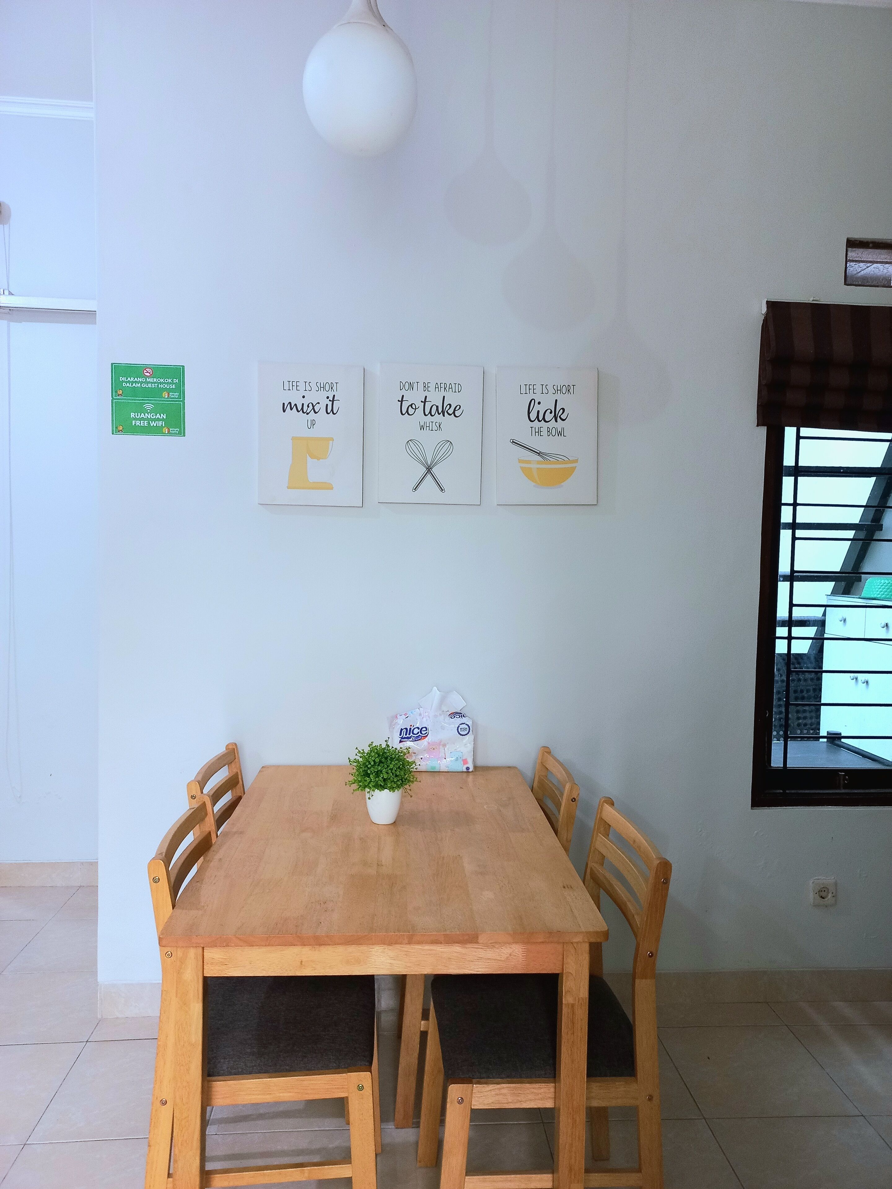 A dining area with a wooden table and chairs, a potted plant, and three motivational wall art pieces.