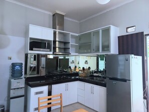 A compact kitchen with white cabinets, a stainless steel range, a microwave, and a refrigerator. - Homestay Jogja Jakal By Simply Homy (Ngaglik)