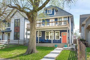 Ein zweigeschossiges Haus mit Veranda, einem großen Baum und einem gepflegten Rasen.
