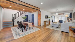 Un amplio salón con una escalera de madera, una mesa de comedor con sillas y un sofá.