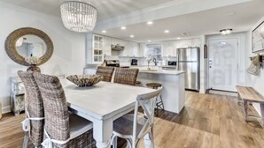 Una cocina moderna con armarios blancos, electrodomésticos de acero inoxidable y un comedor con sillas de mimbre y un candelabro.