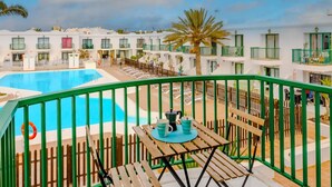 A balcony with a pool, wooden furniture, and white buildings in the background.