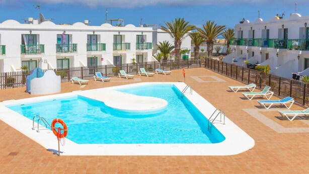 A rooftop pool with lounge chairs and a white building with balconies.