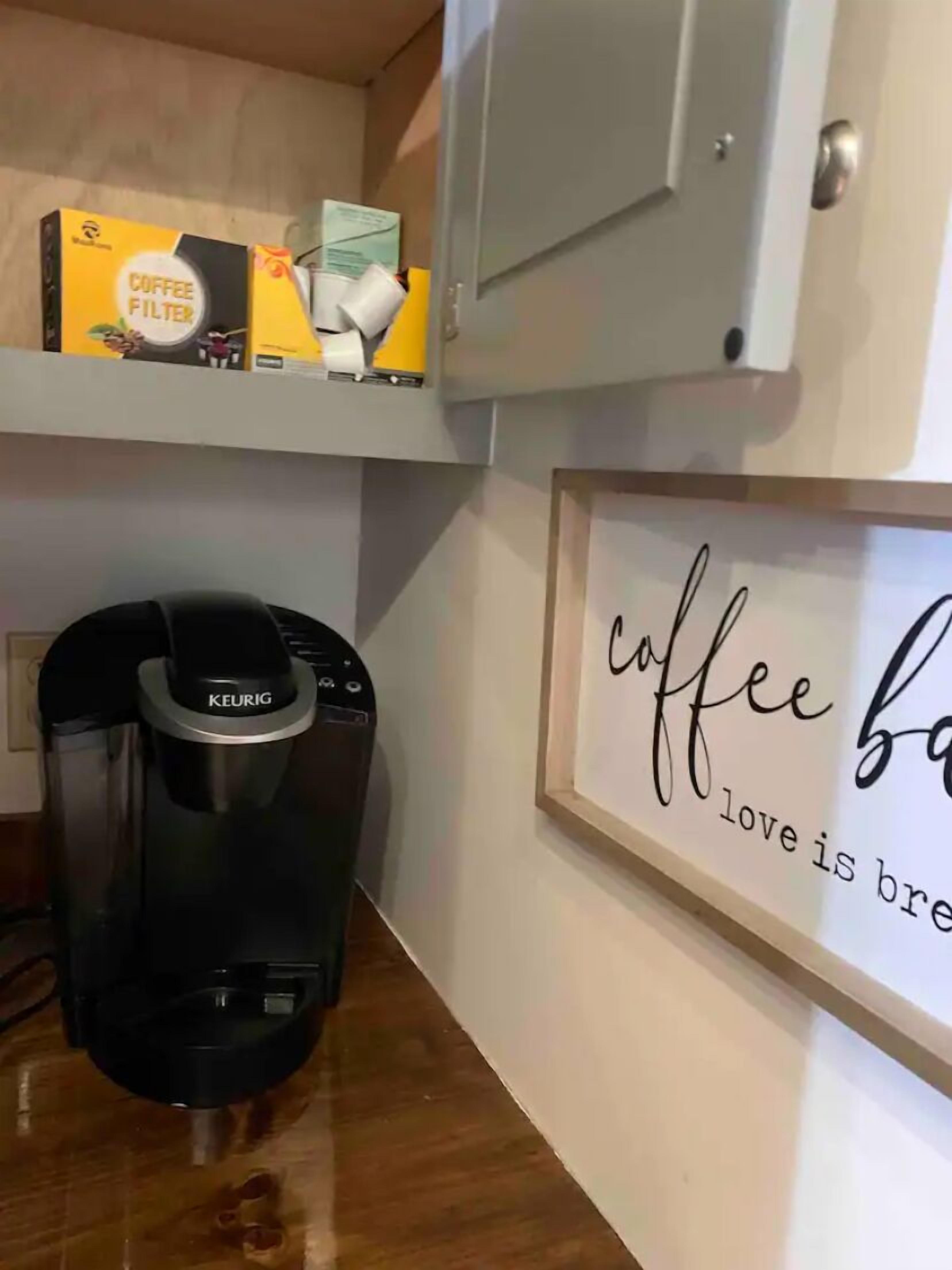 A kitchen with a Keurig coffee maker, a coffee filter box, and a framed sign saying "coffee is love is brew".
