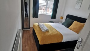 Una habitación de hotel con cama, ventana con cortinas, radiador y puerta.